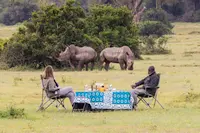 A couple relaxing and drinking watching two rhinos on luxury safari in Kenya