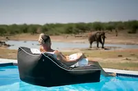 Photo of traveller sitting in swimming pool watching Elephants at a watering hole on Safari in Africa